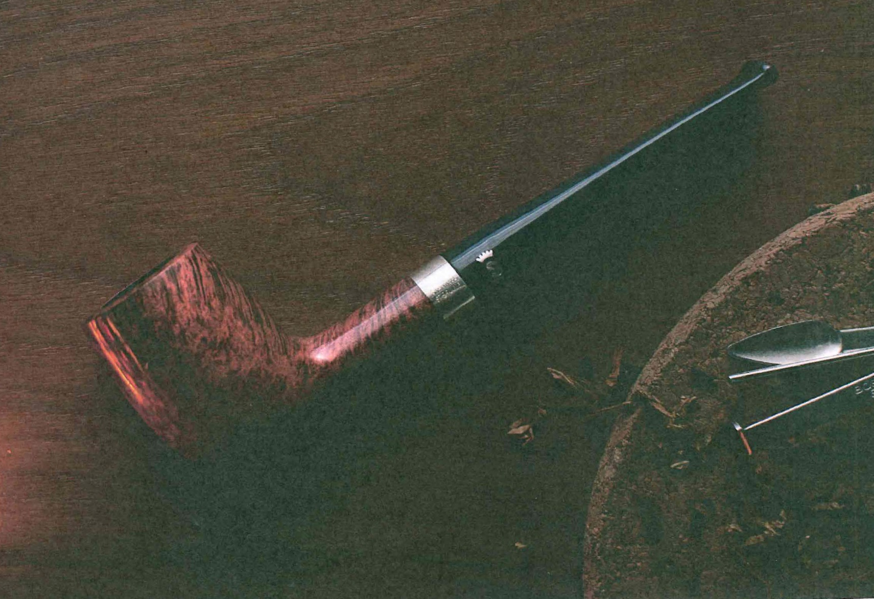 Mood Bild einer geraden rötlichen Stanwell Pfeife mit Silberring neben Pfeifenbesteck